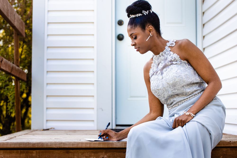 Wedding guest in white lace dress signing document while seated on wooden porch steps.