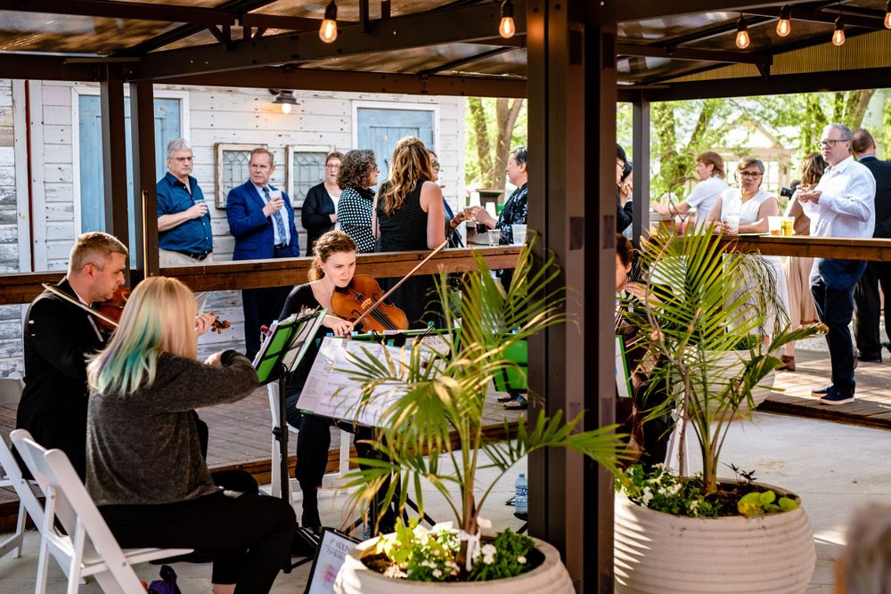 Wedding reception setting under covered patio with tropical plants and white table settings.
