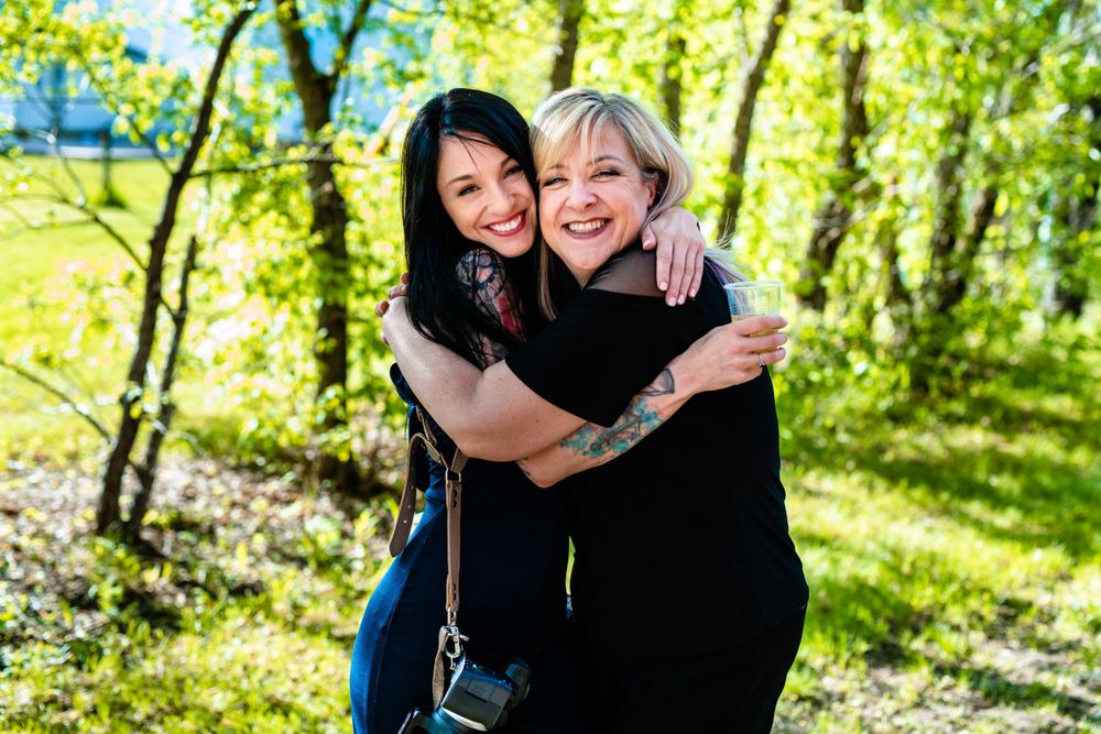 Two people embracing and smiling outdoors in a sunlit wooded area on a bright sunny day.