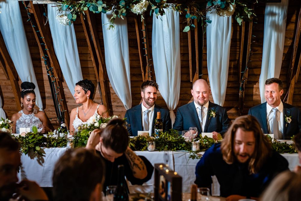 Wedding party seated at decorated head table during reception celebration.