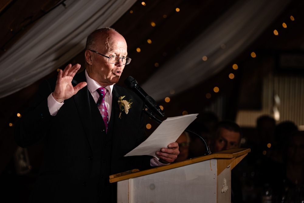 Speaker delivering speech at podium during evening wedding reception.