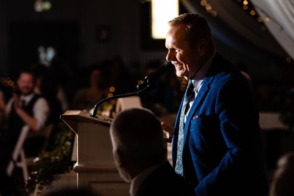 Man in blue suit giving speech at illuminated podium during evening event.