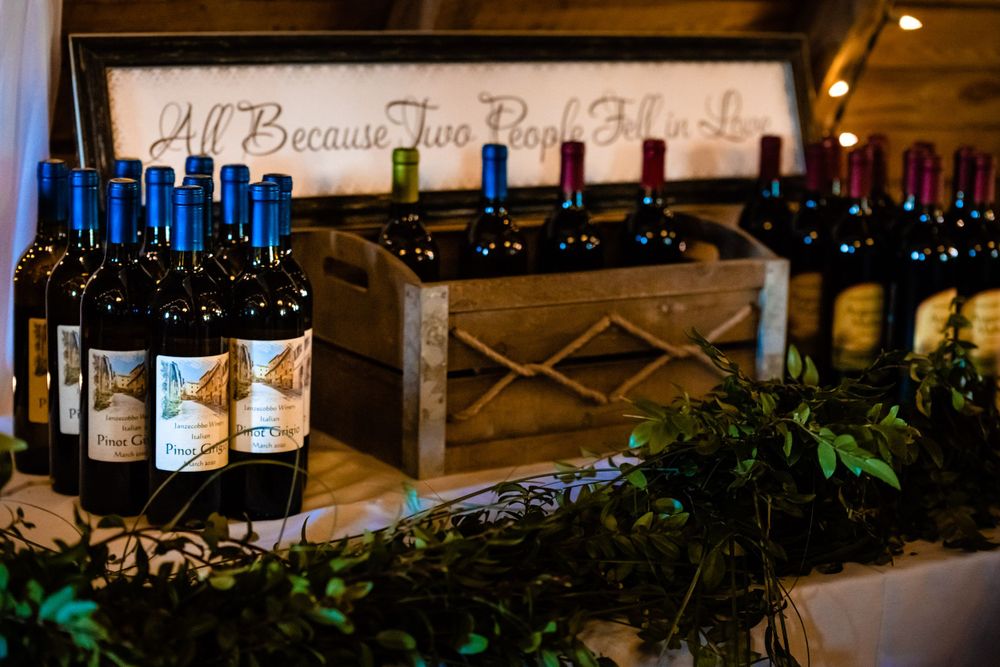 Array of wine bottles displayed with greenery at wedding reception bar setup.