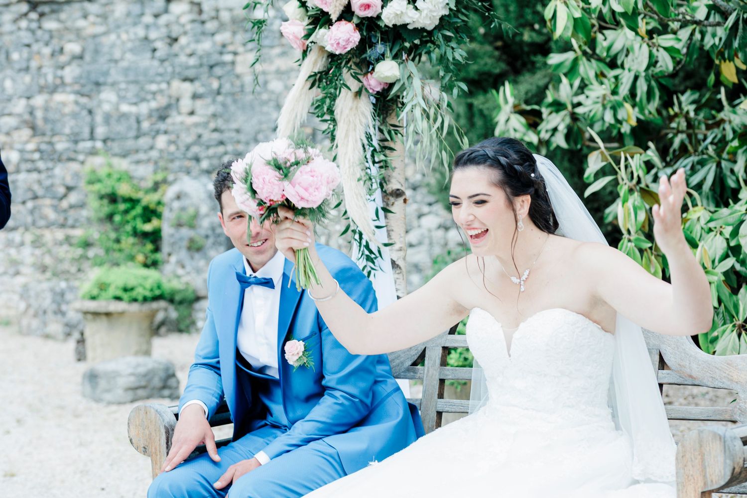 Wedding celebration at stone wall garden with floral arch and outdoor seating.