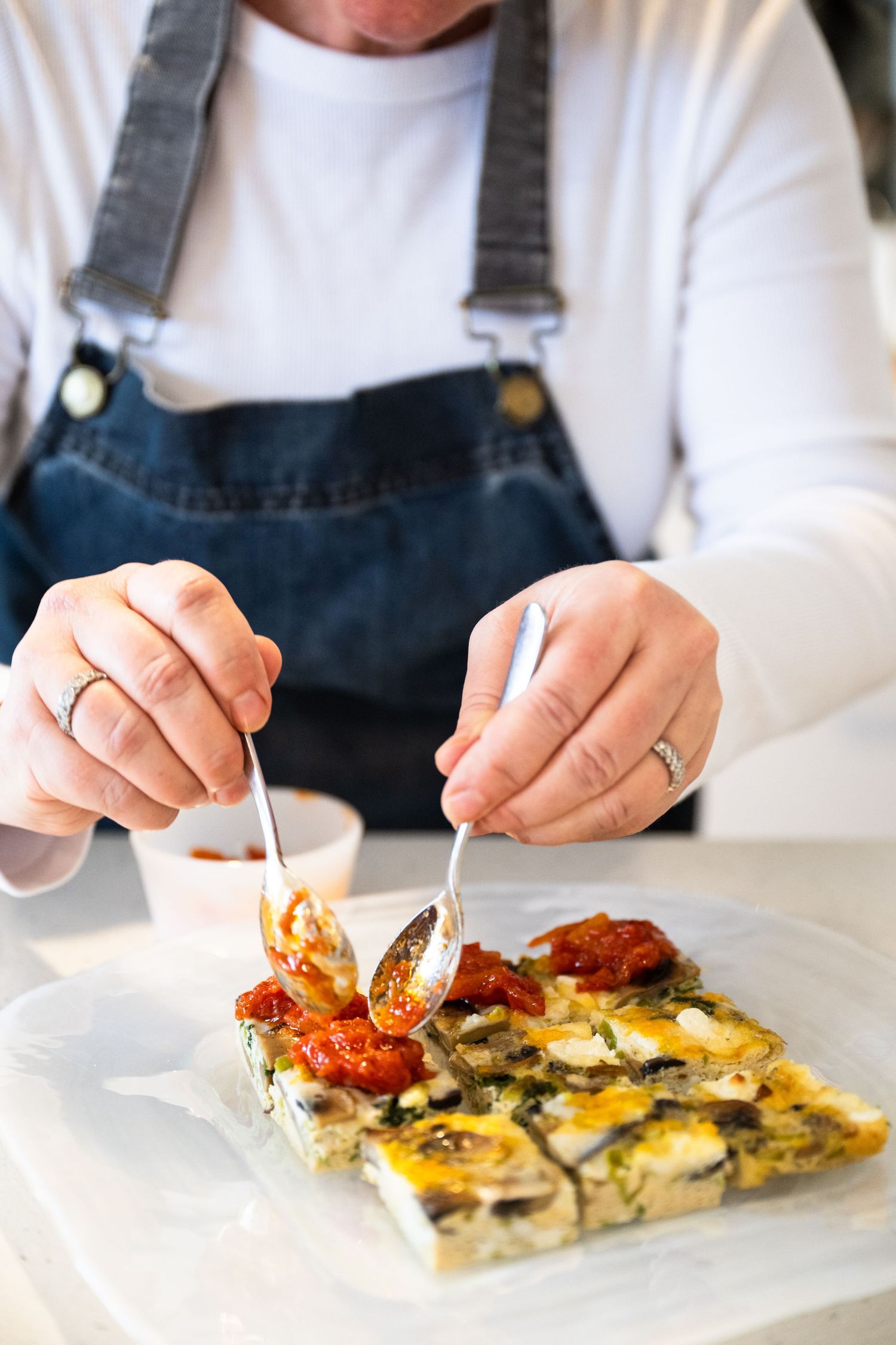 Close-up view of hands in denim apron cutting into a savory tart with roasted tomatoes and mushrooms on white plate.
