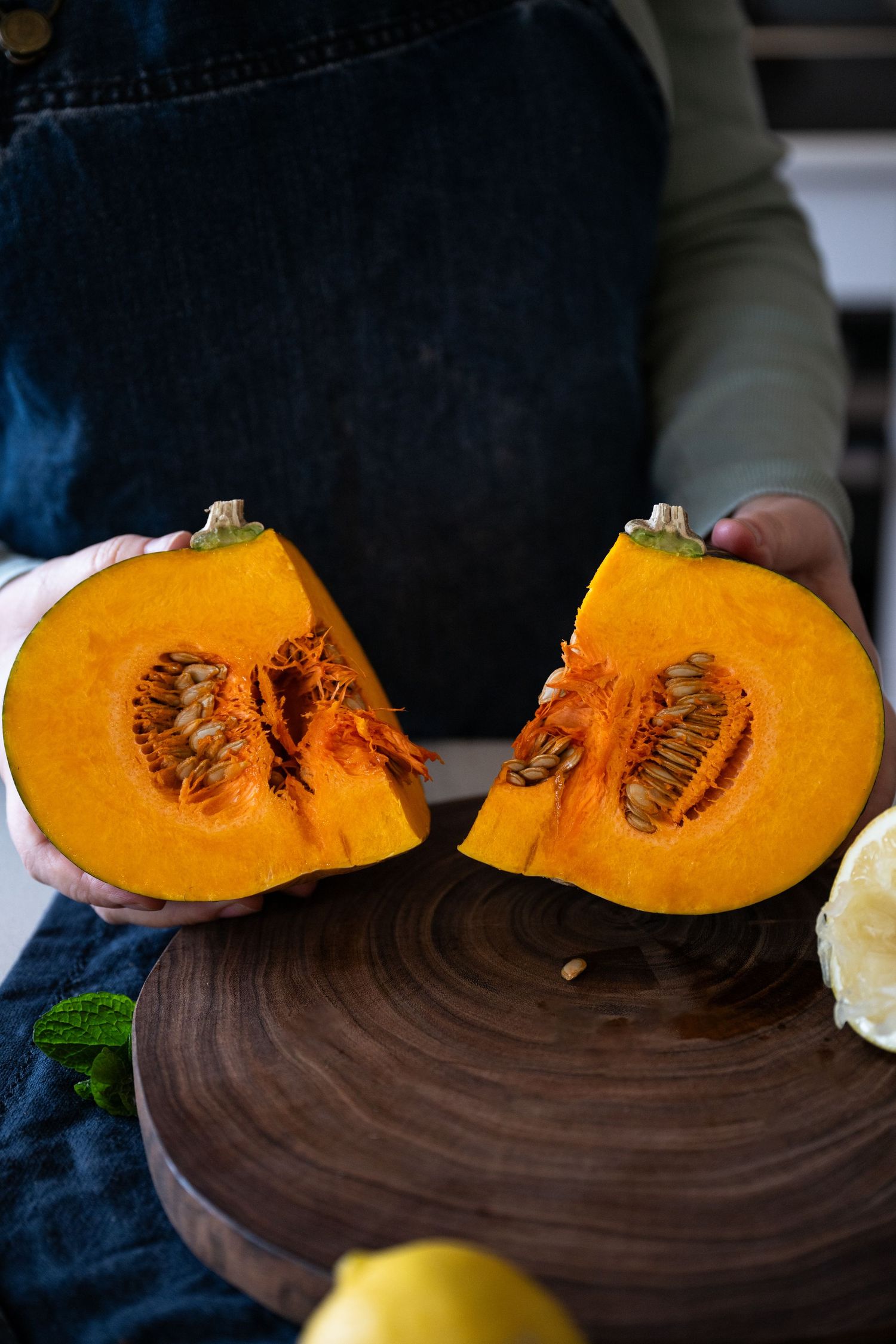 Halved fresh orange pumpkin showing vibrant flesh and seeds on a dark wooden cutting board.
