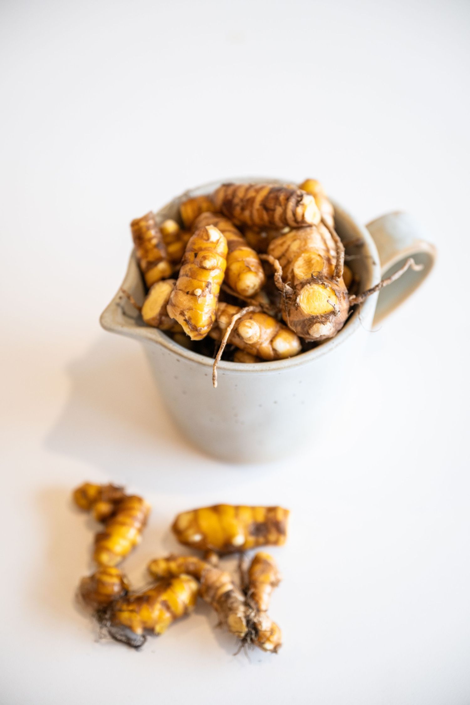 Fresh turmeric root with golden orange color displayed in a small metal bucket on white background.