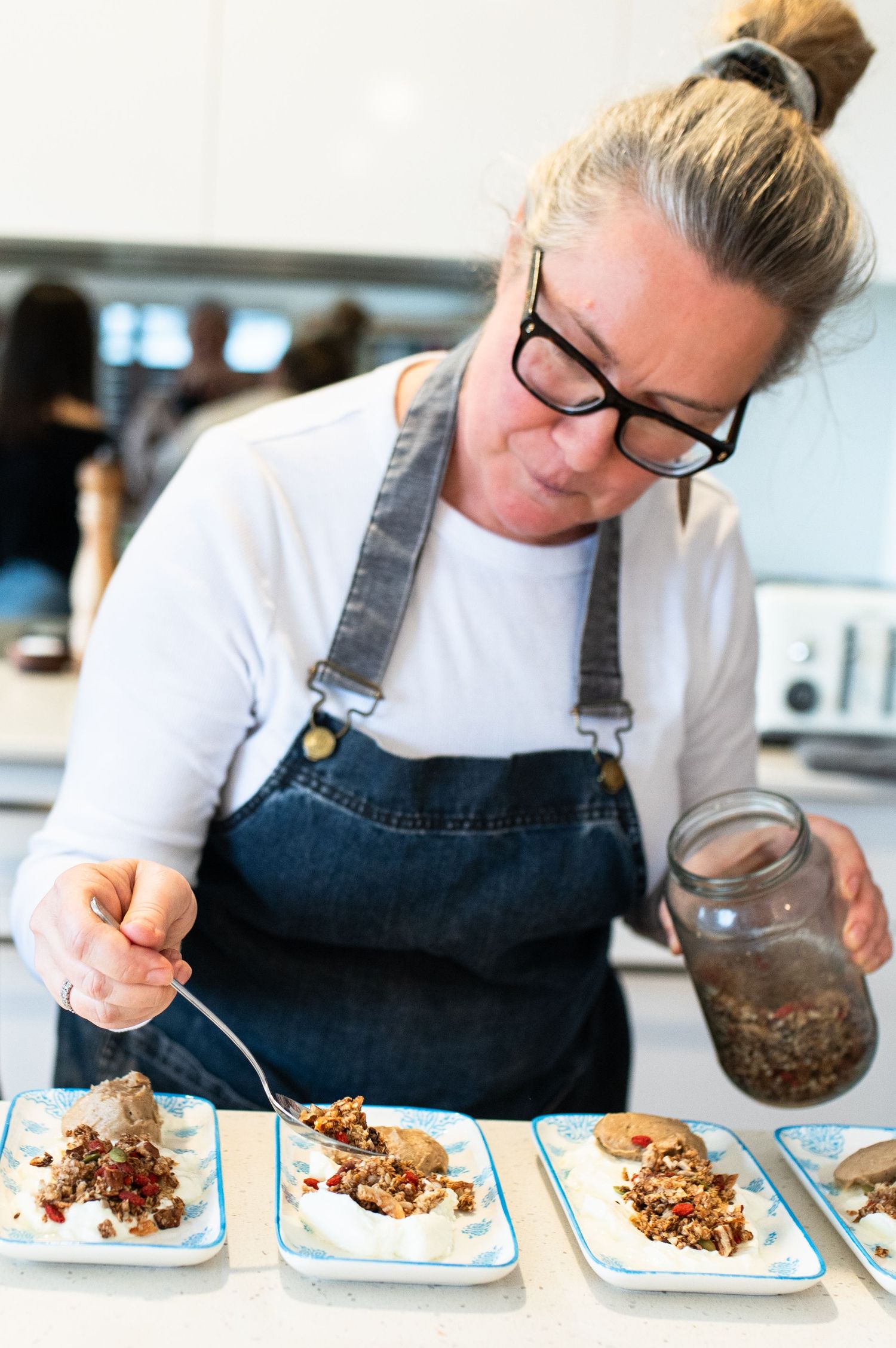 Chef in apron and glasses carefully plates multiple dishes in sequence on light blue square plates.