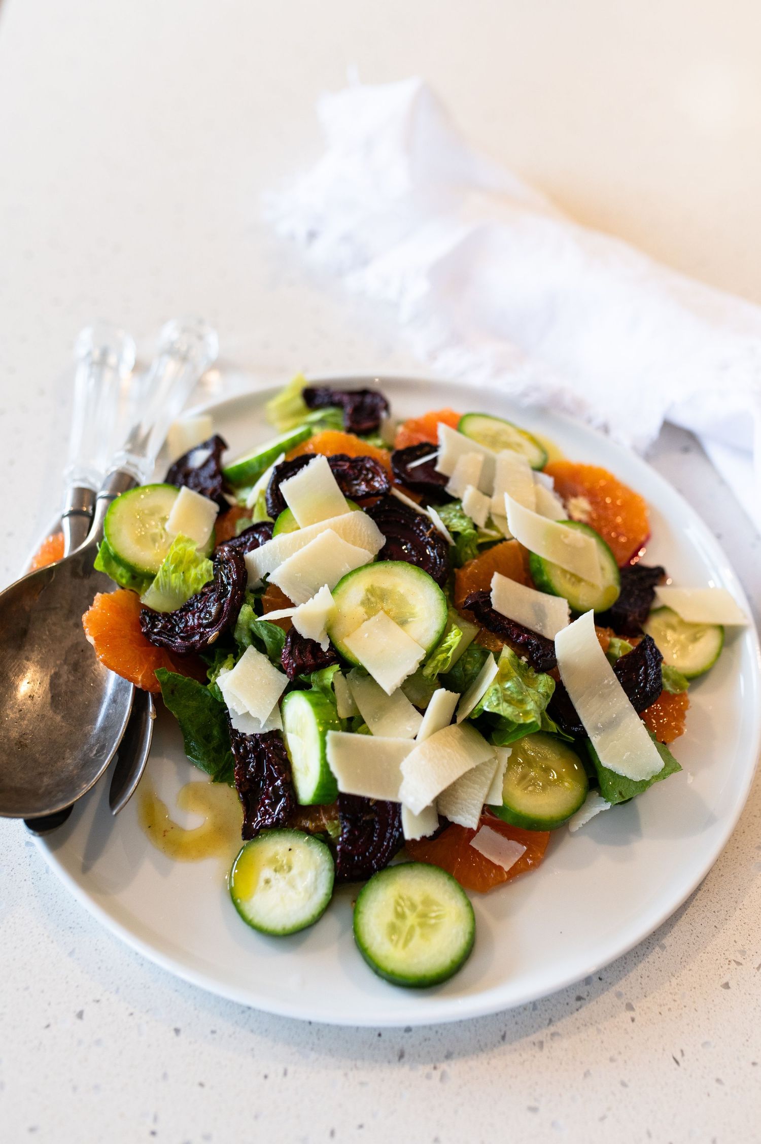 Fresh Mediterranean salad with sliced cucumbers, tomatoes, olives and shaved parmesan on a white plate.