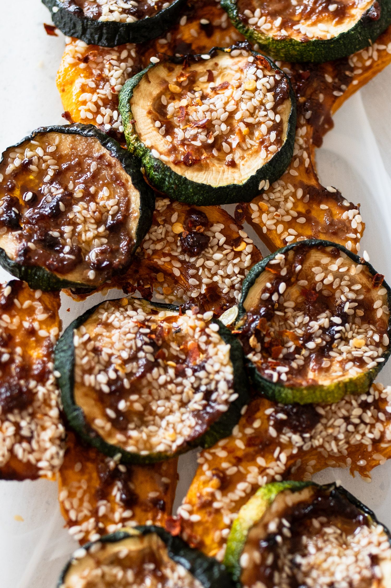 Grilled zucchini slices topped with sesame seeds and a sweet glaze served on a white plate.