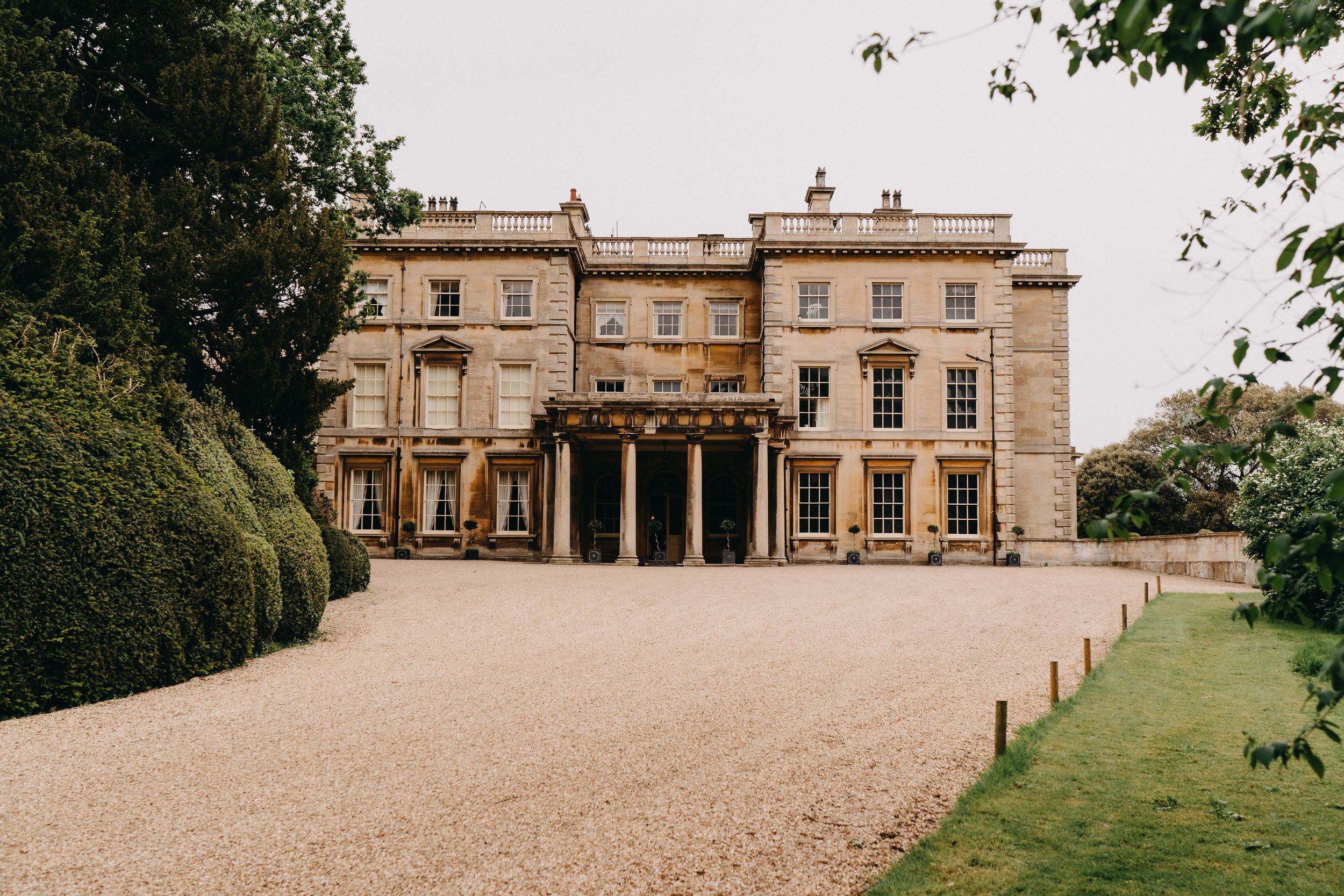 Grand historical mansion of Prestwold Hall with columned portico entrance and gravel driveway surrounded by manicured gardens.
