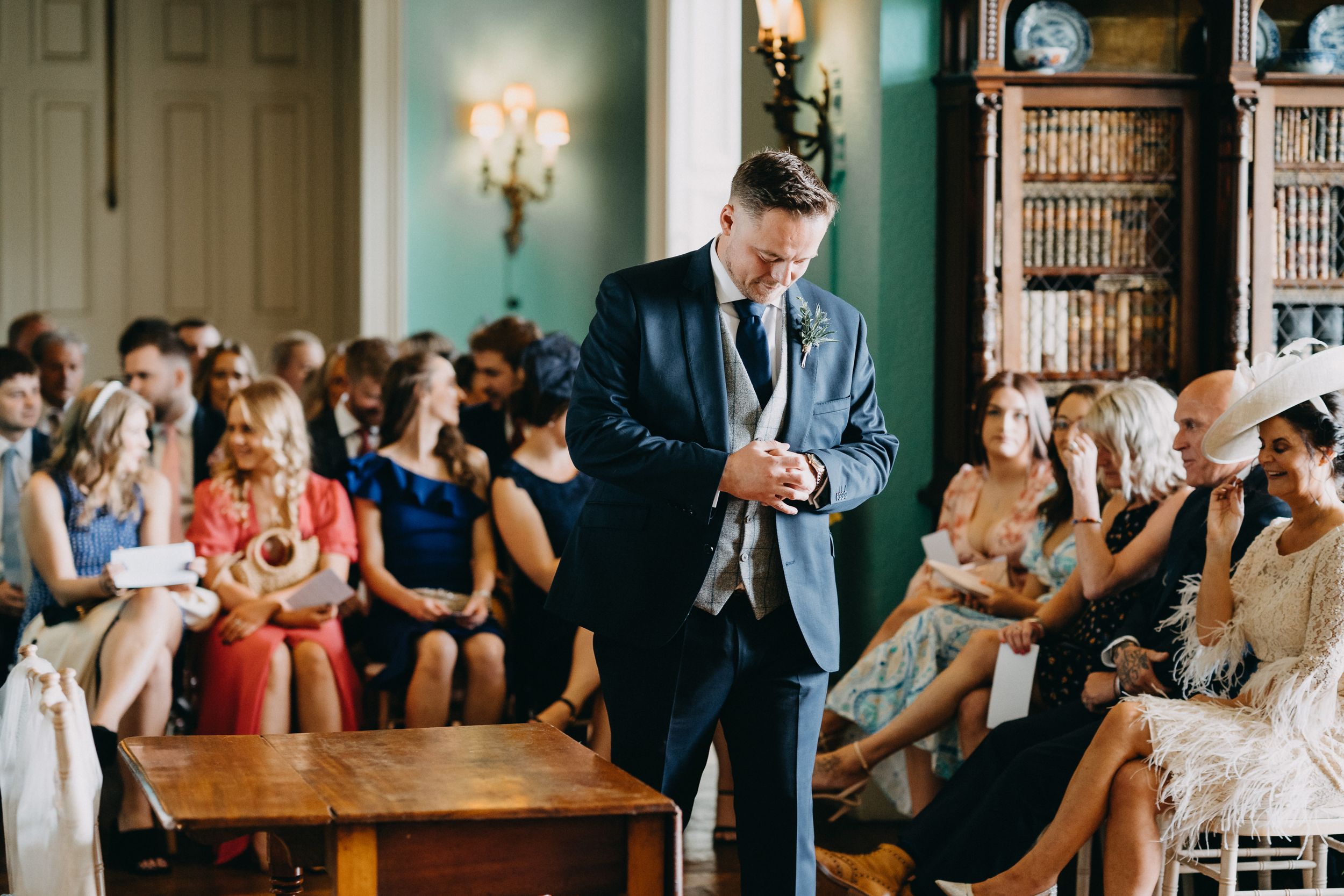 Guest speaker delivers a presentation to an attentive audience in a room with blue-green walls and wall sconces.