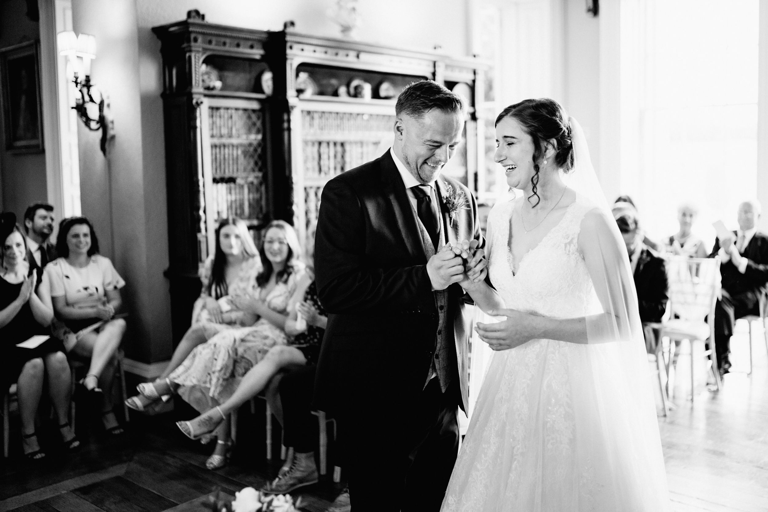 A black and white photo capturing a tender moment between newlyweds during a wedding ceremony with guests looking on.