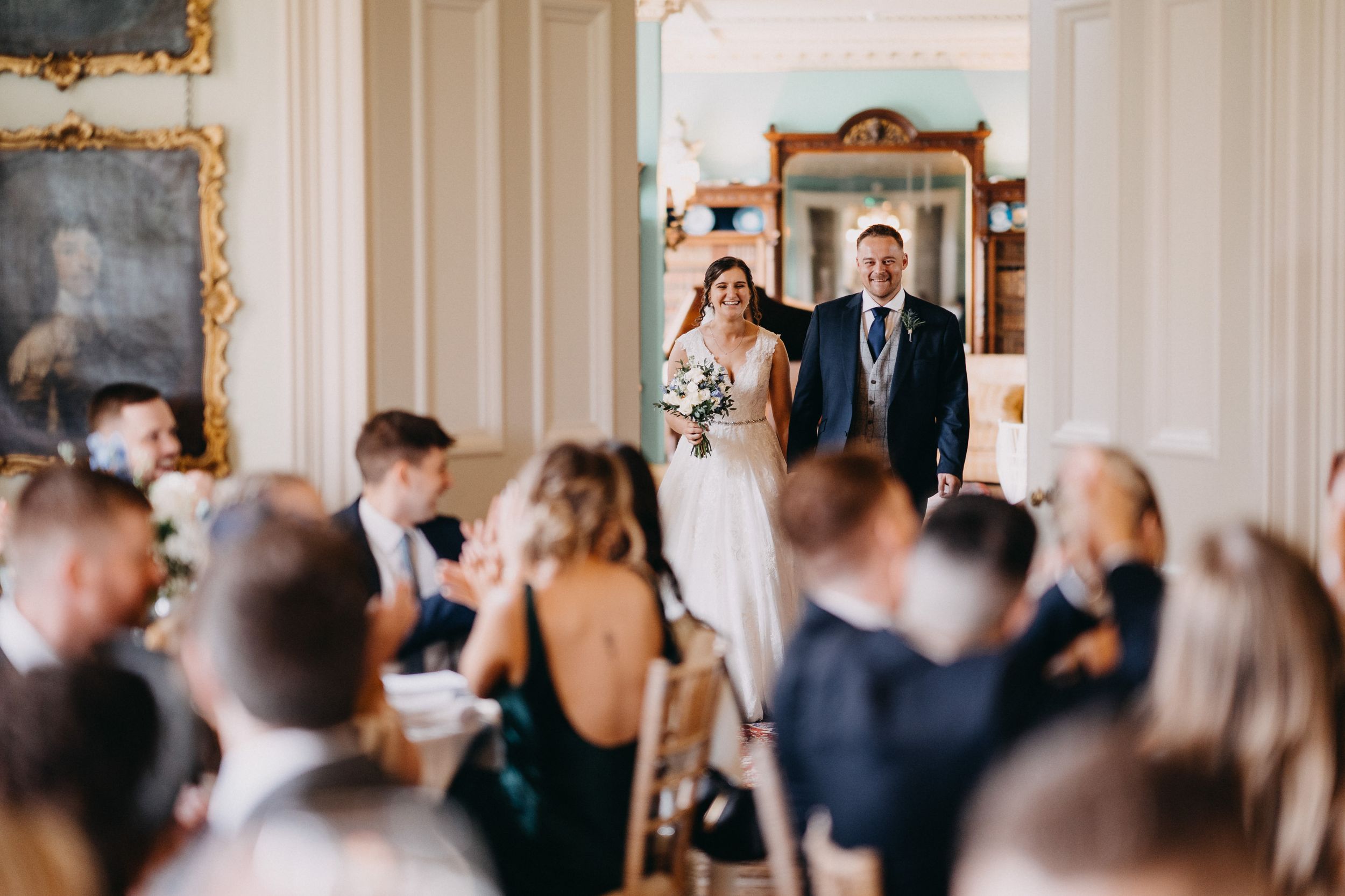A wedding ceremony in an elegant room with ornate gold-framed mirrors and guests seated in formal attire.