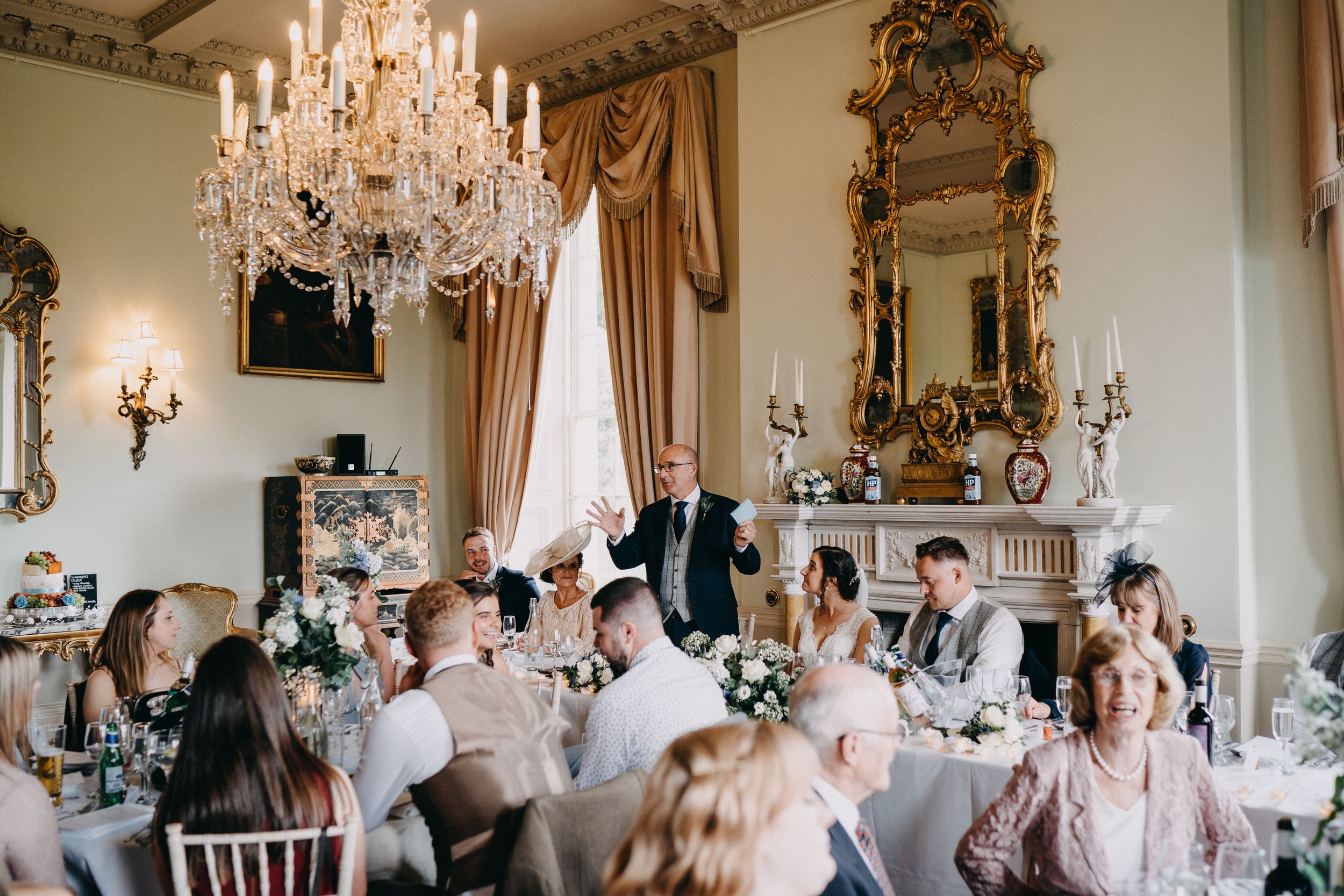 Guests seated at dining tables in an ornate historic room with crystal chandeliers and gilded mirrors.