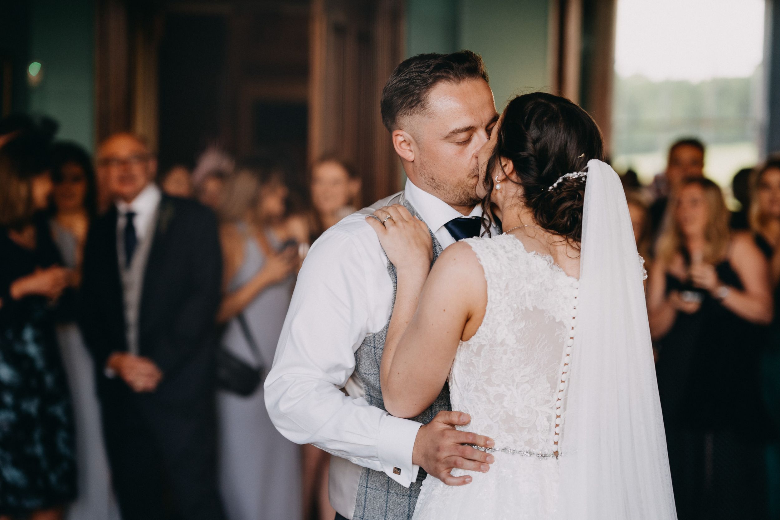 A couple shares an intimate moment during their wedding reception with guests in the background at a venue.