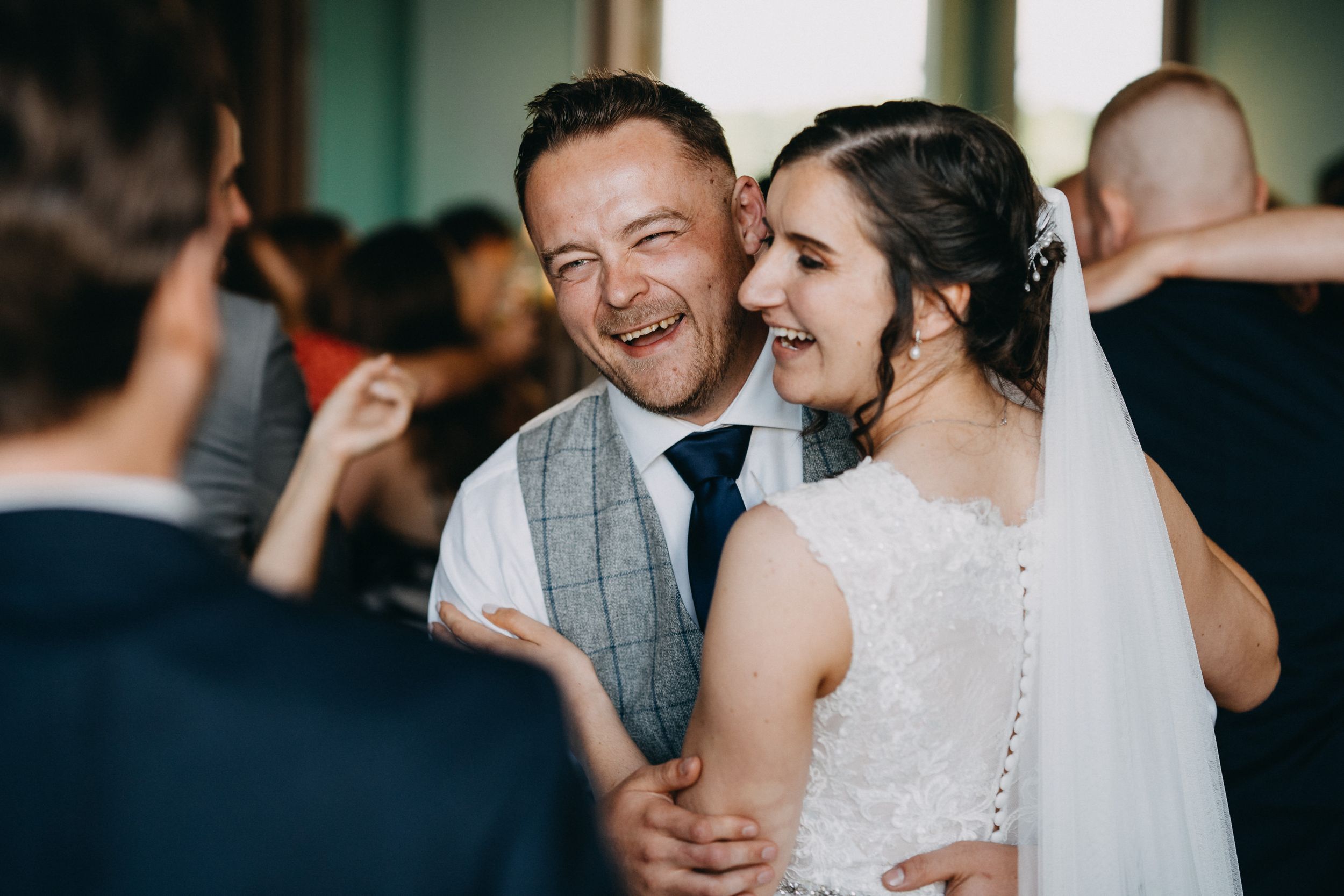 Candid moment captured at a wedding celebration with guests sharing laughter in an indoor venue.