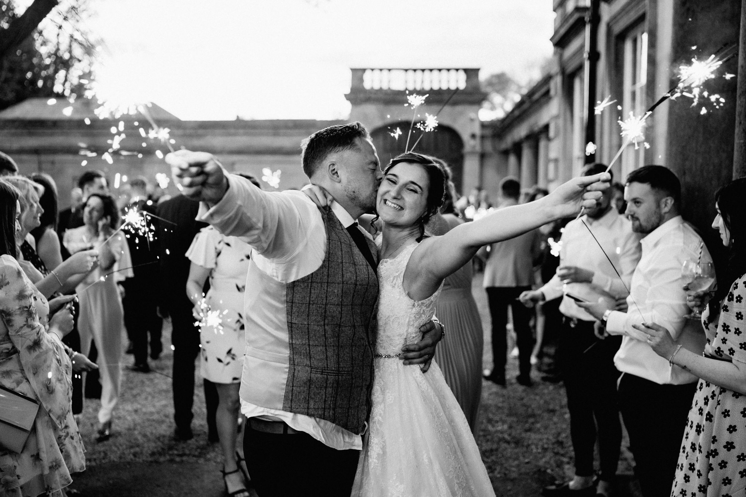 Joyful couple at outdoor wedding celebration strikes enthusiastic pose while dancing among guests.