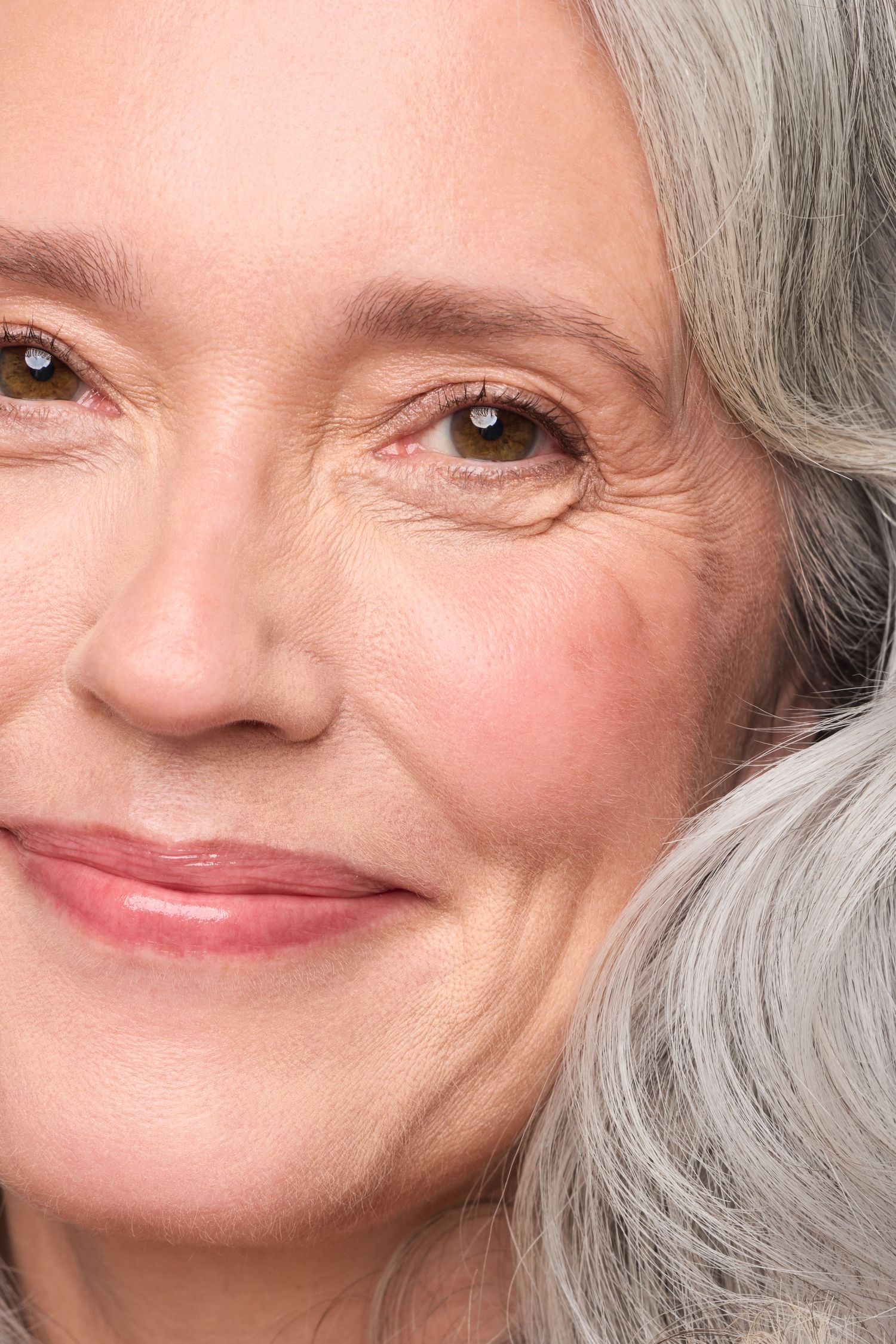 Close-up portrait showing a warm smile and natural gray hair against neutral background.