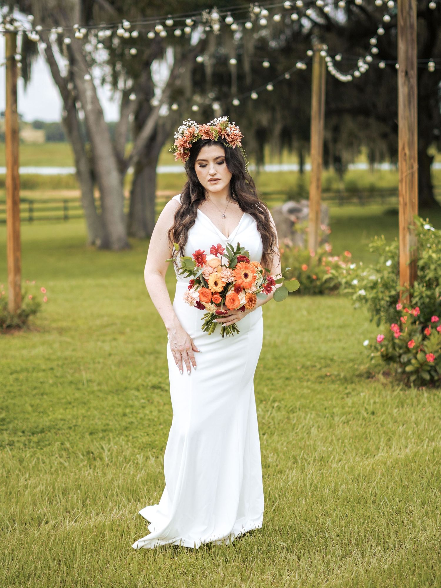Garden bridal portrait under string lights featuring white gown and coral floral accessories.