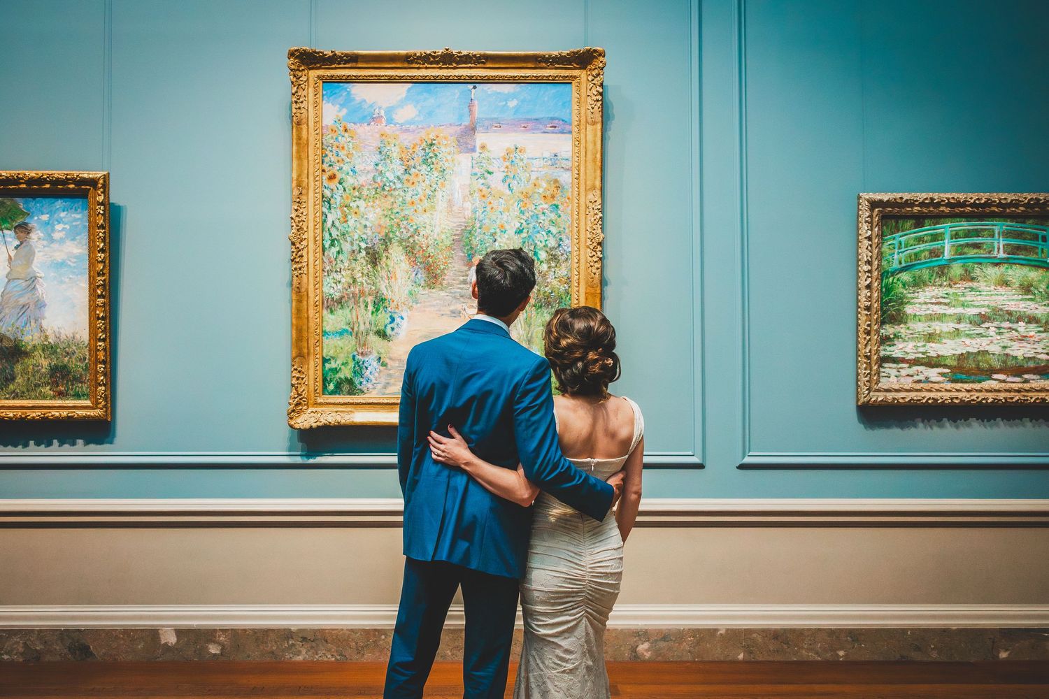 A couple views artwork in a gallery with turquoise walls and gold framed Monet paintings at the National Gallery of Art In DC