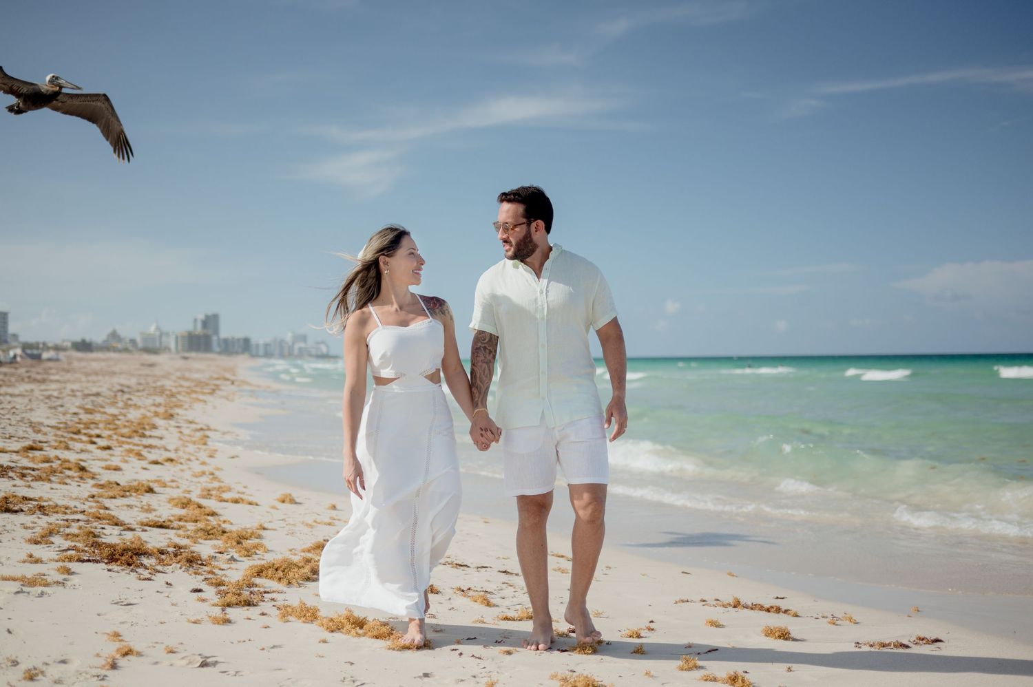 Romantic beachside photo series showing a couple in white outfits walking along a pristine tropical shoreline in Miami.