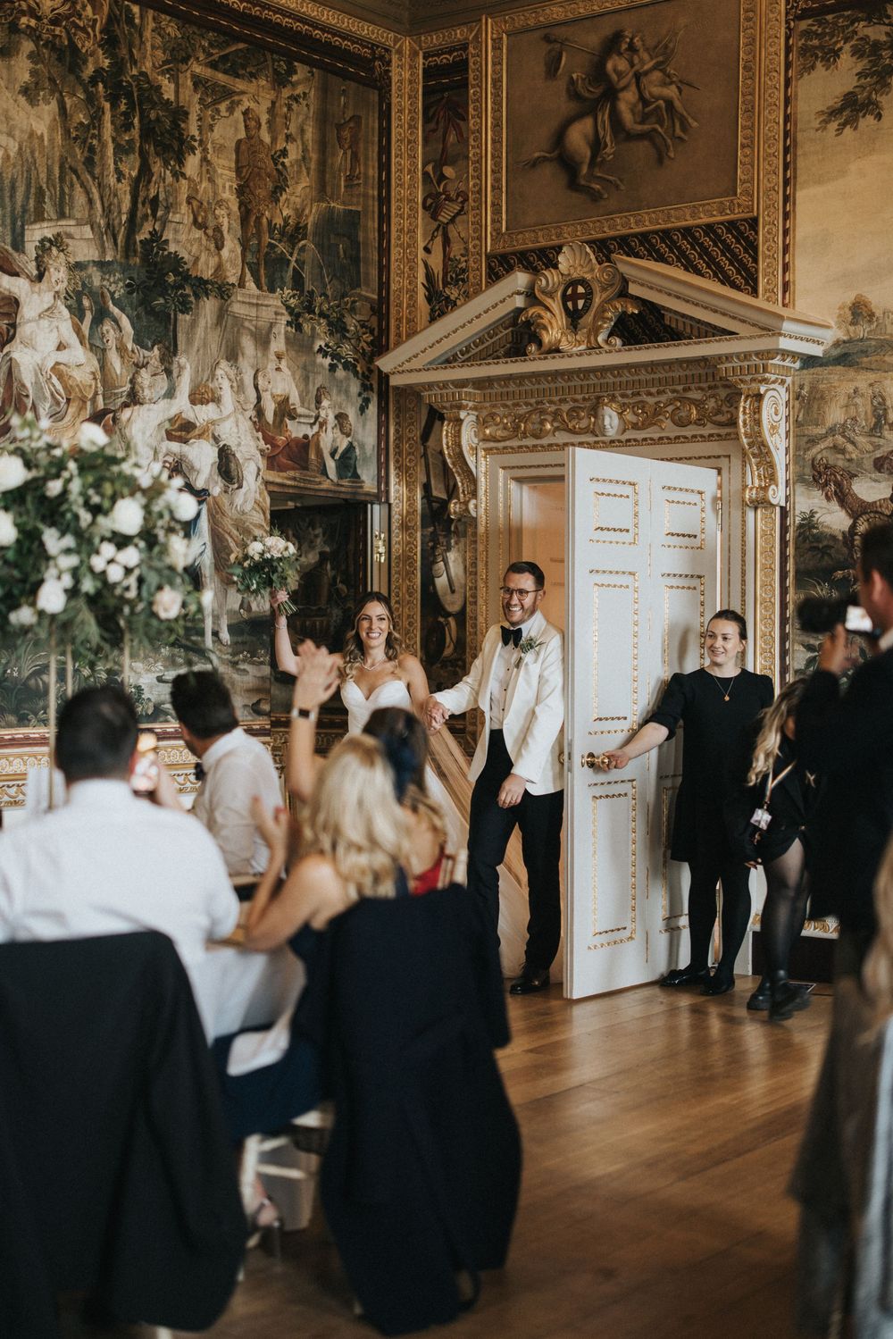 Elegant wedding celebration in an ornate historic room with grand murals and classical architectural details during a reception.