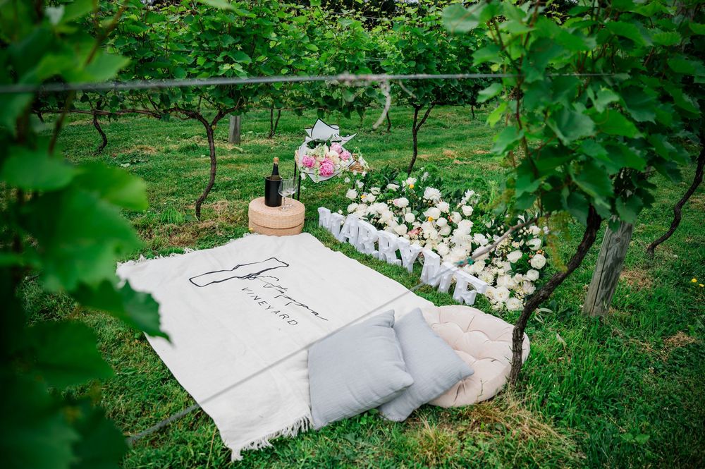 A mattress with white bedding lies in a green garden setting with flowers and vegetation.