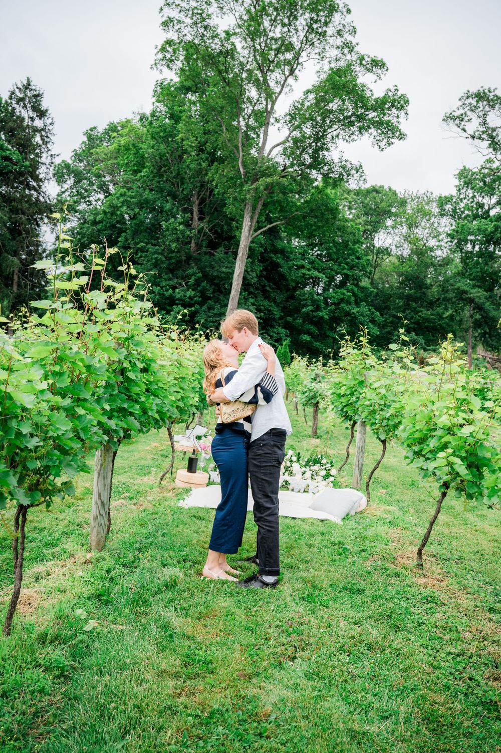 A romantic moment between a couple embracing in a lush vineyard setting during a summer day.