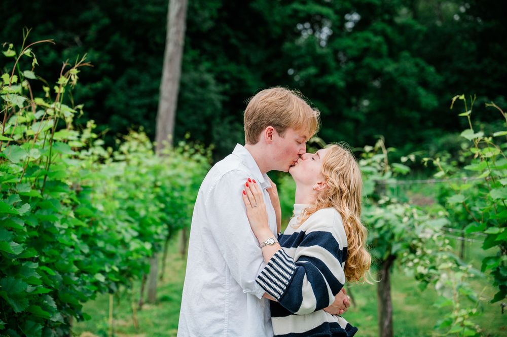 A romantic couple embraces and shares a kiss in a lush garden setting with green foliage in the background.