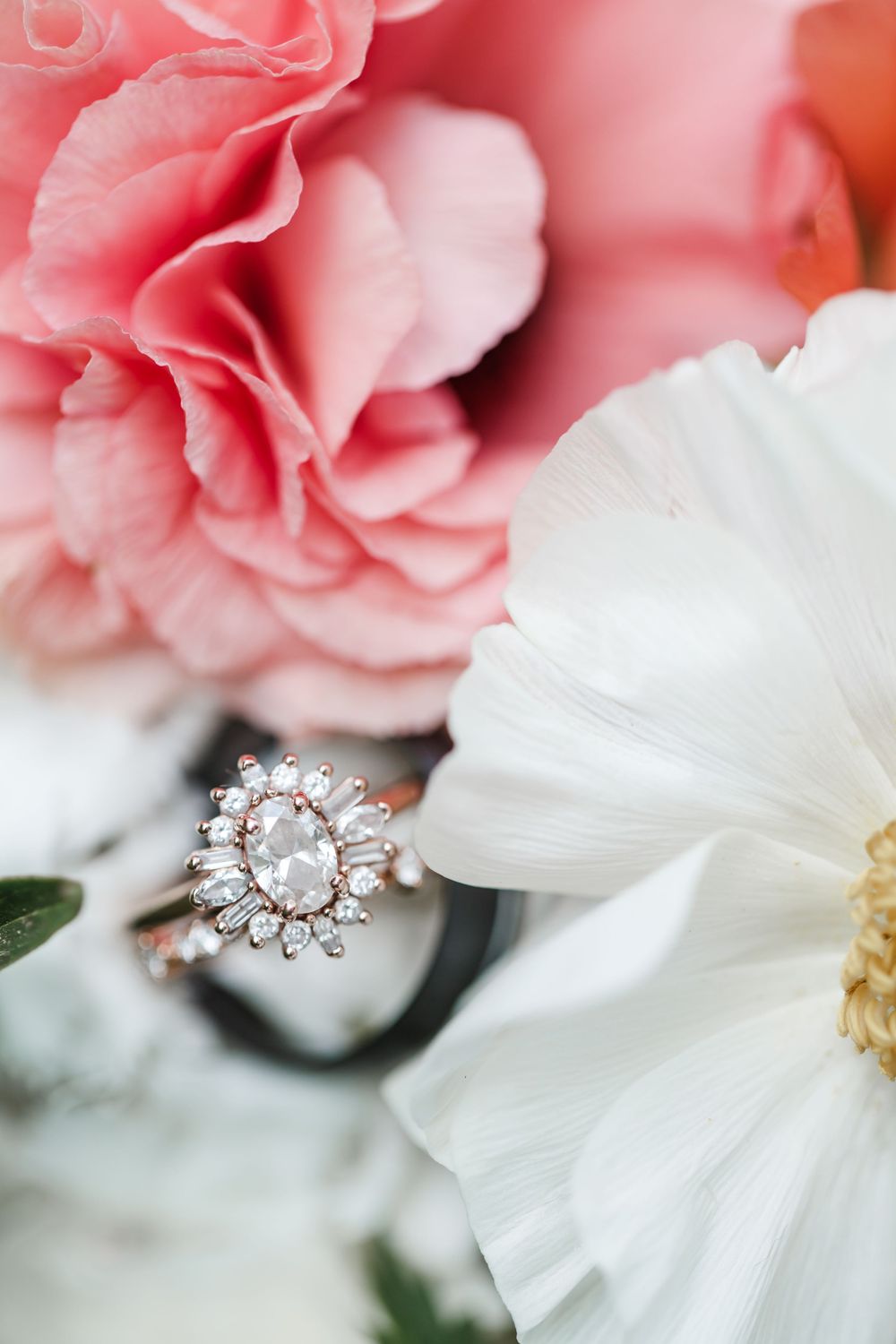 An elegant diamond engagement ring with halo design nestled among pink and white flowers with soft petals.