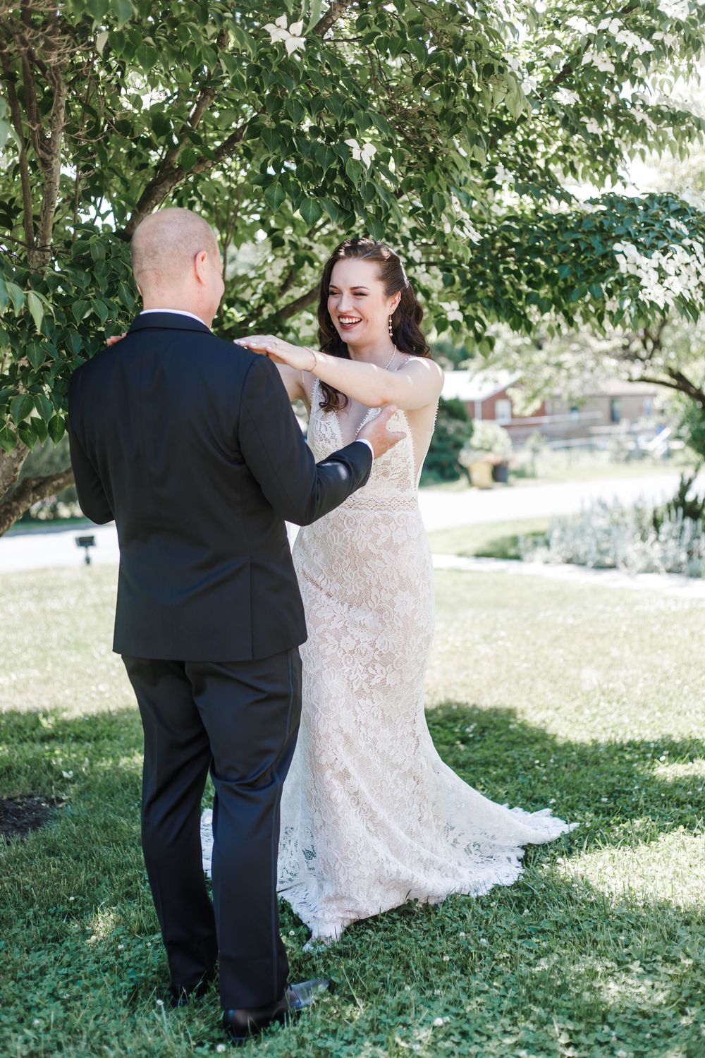 A couple shares a romantic first dance outdoors under green trees at their wedding celebration.