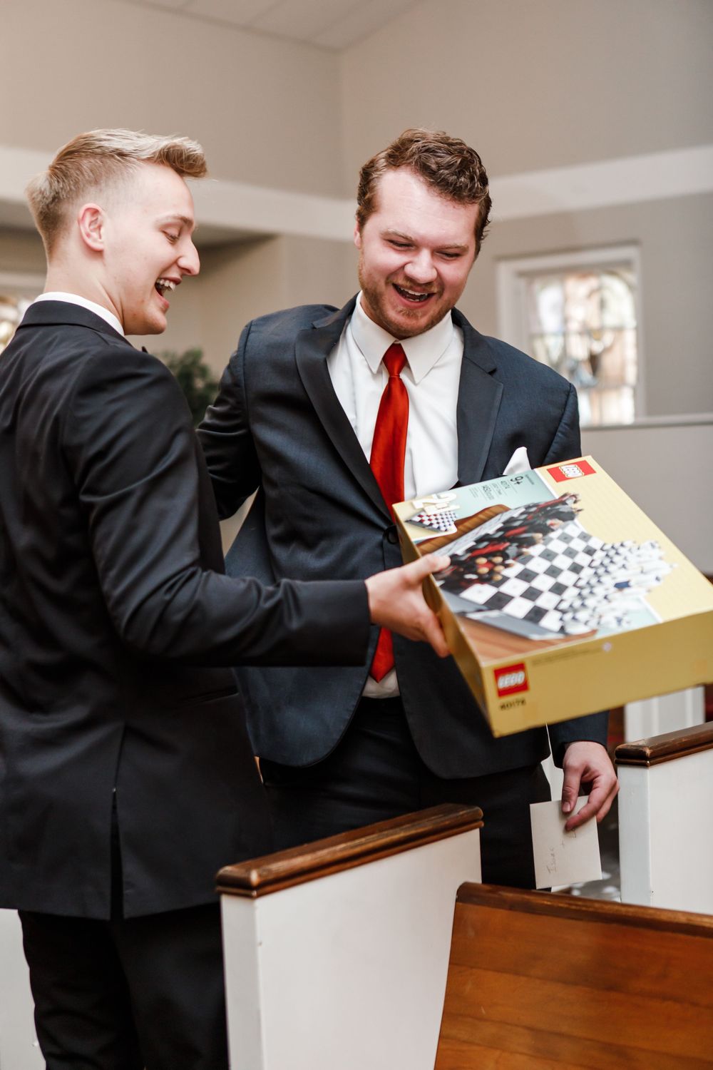 Two men in suits share a joyful moment while looking at a chess set in a box.