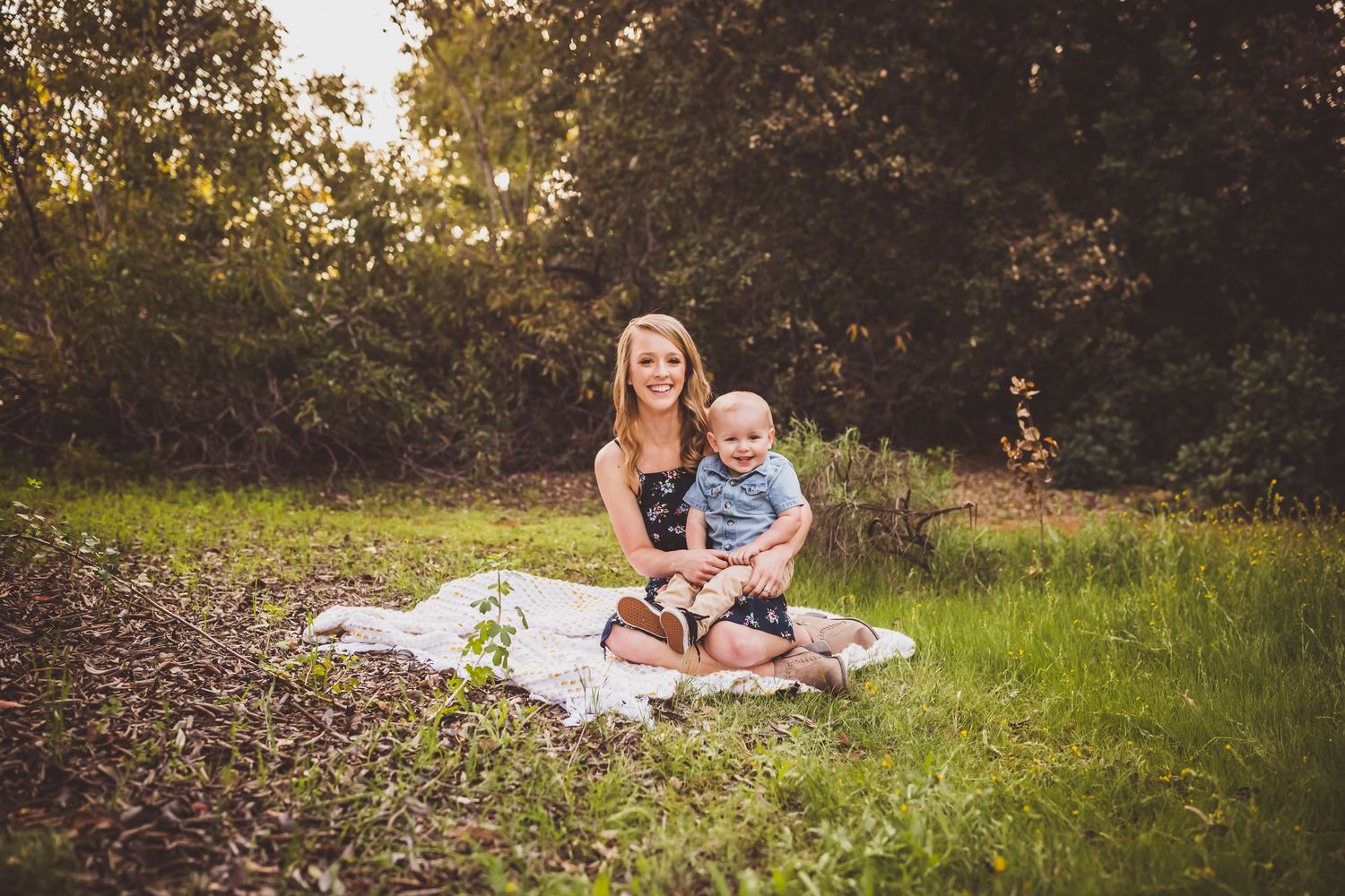 A peaceful outdoor photoshoot on a white blanket in a grassy field during golden hour.
