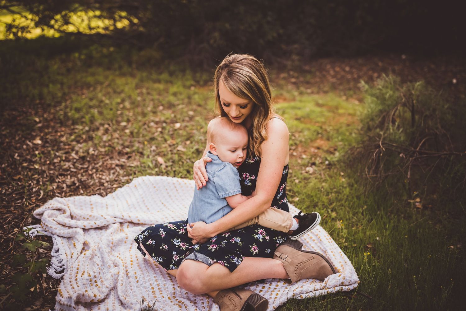 A tender moment of nursing on a white blanket outdoors in a natural wooded setting on an autumn day.