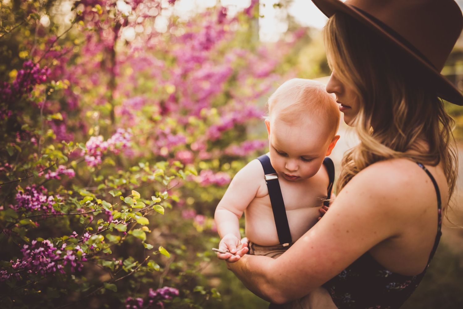 Beautiful outdoor photoshoot in a garden with pink blossoms and a brown hat at sunset.