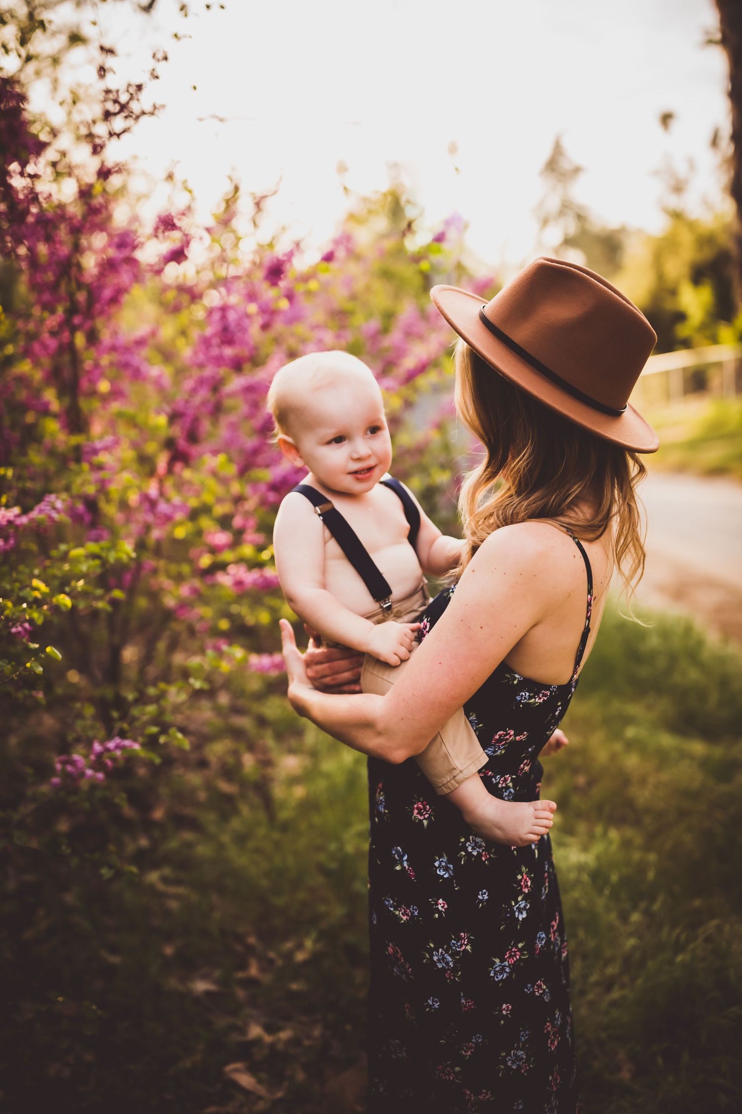 A sunset portrait in a garden with blooming pink flowers and wearing a brown fedora hat.