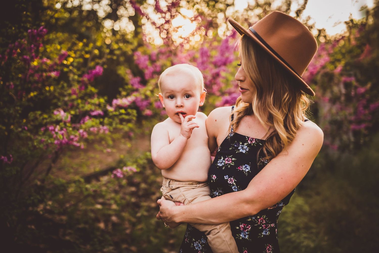 Floral garden photoshoot featuring a brown hat and floral dress among pink blooming trees at sunset.