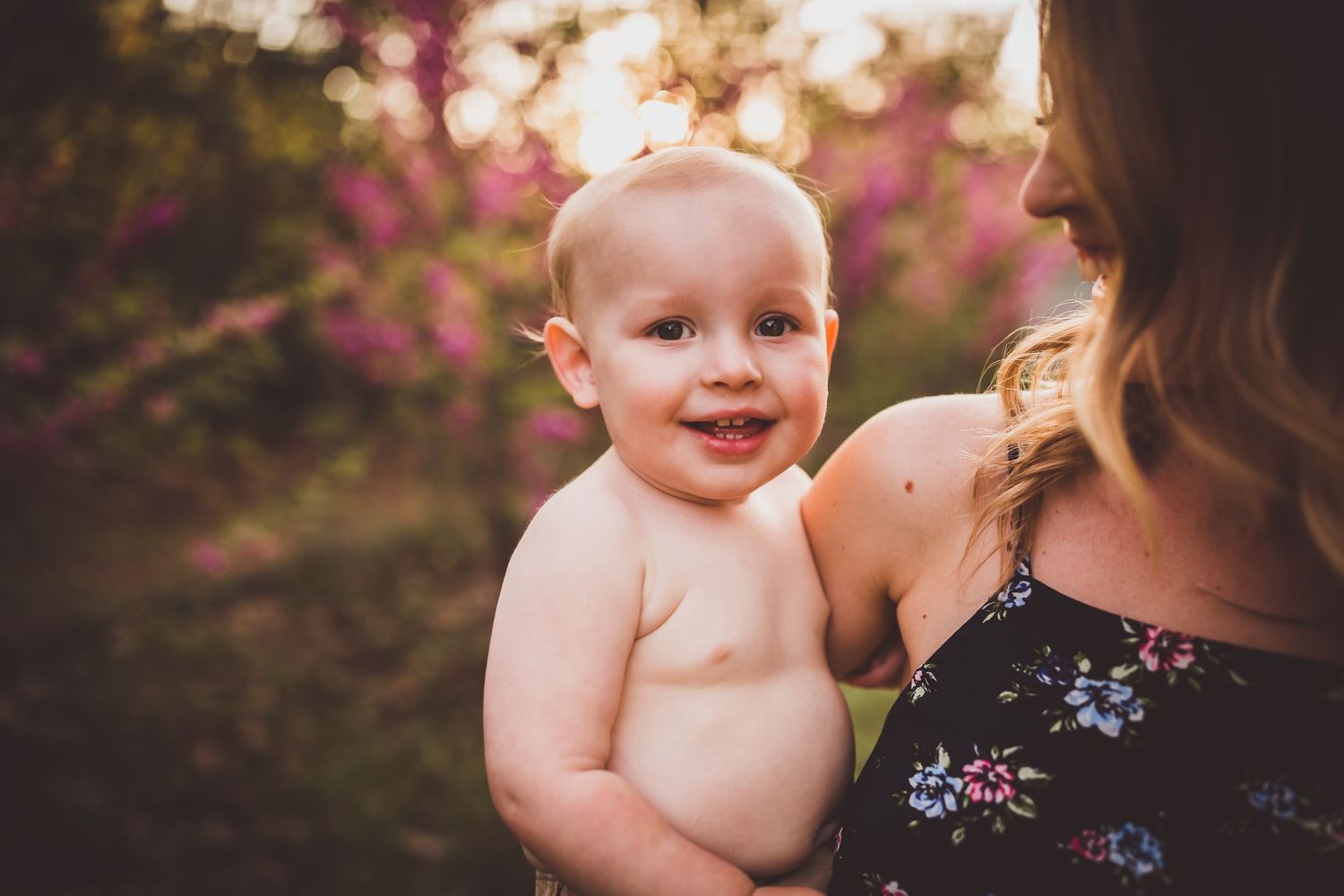 A close-up portrait outdoors with pink flowering trees in soft focus behind.