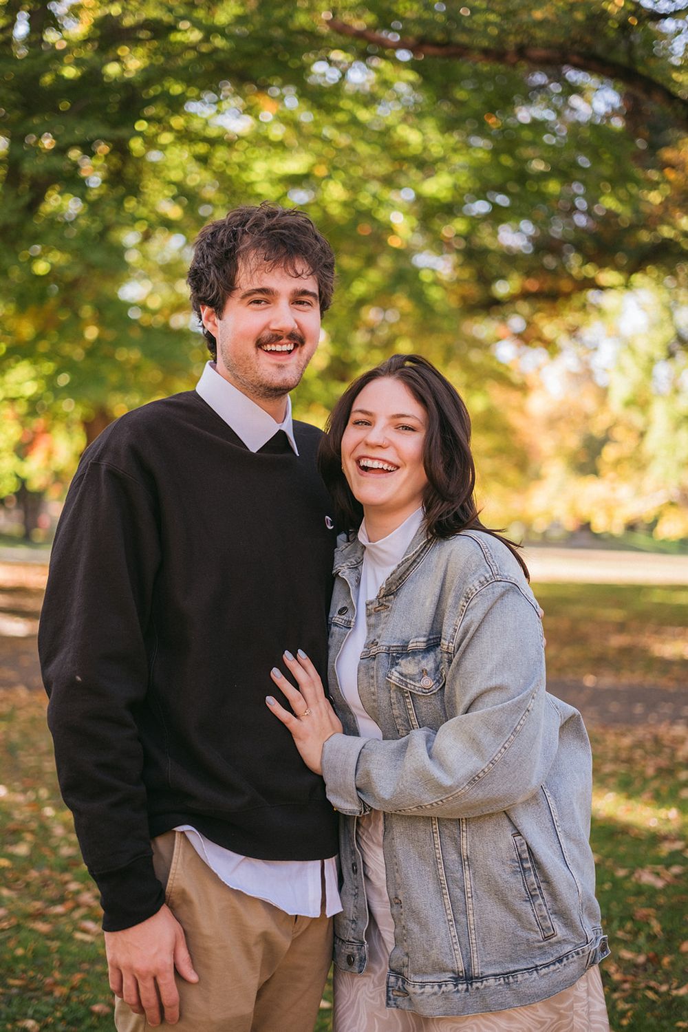 A couple sharing a joyful moment together on an autumn day with golden foliage in the background.