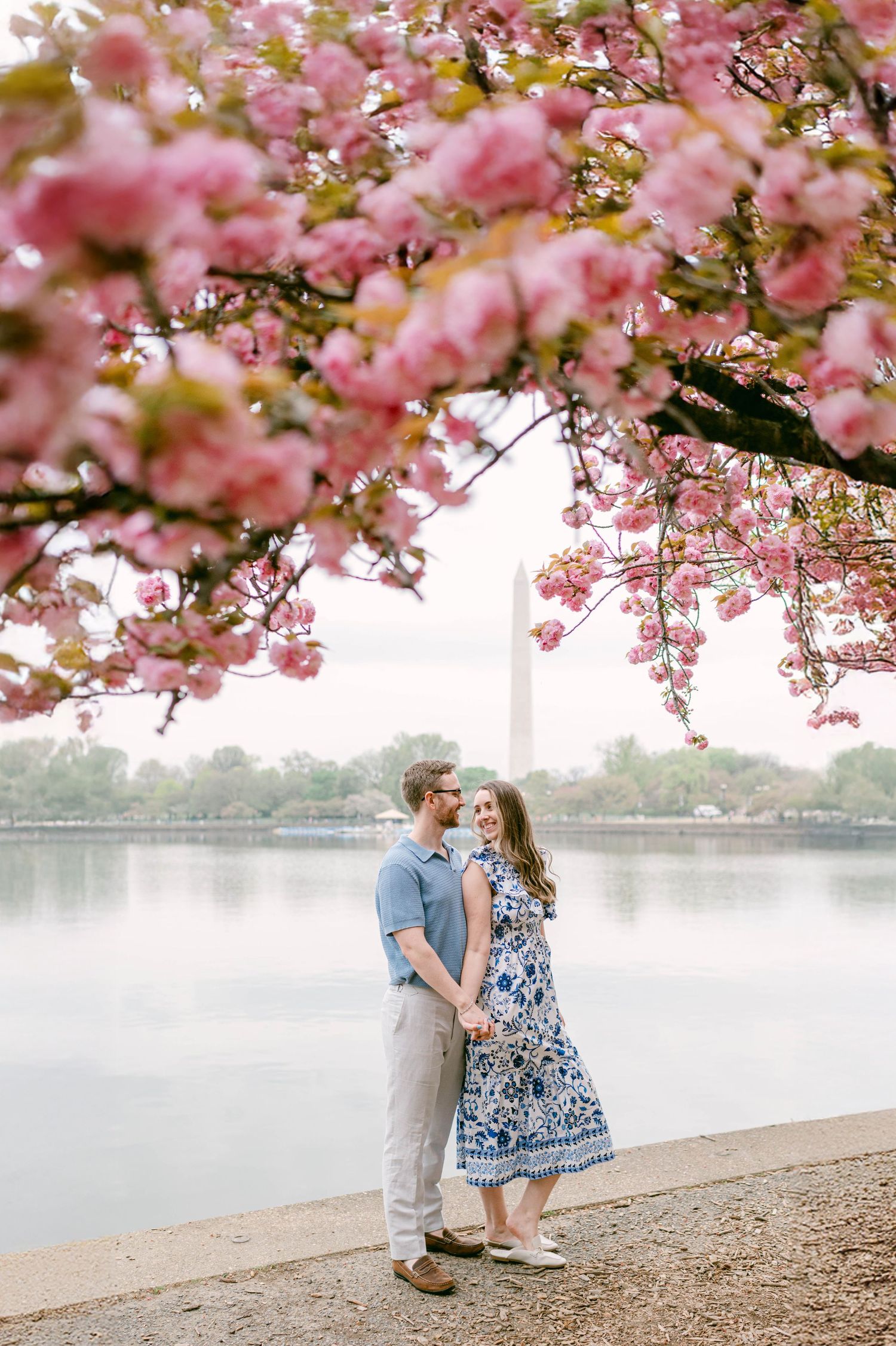 Cherry blossoms frame couple beneath Washington Monument by Tidal Basin.