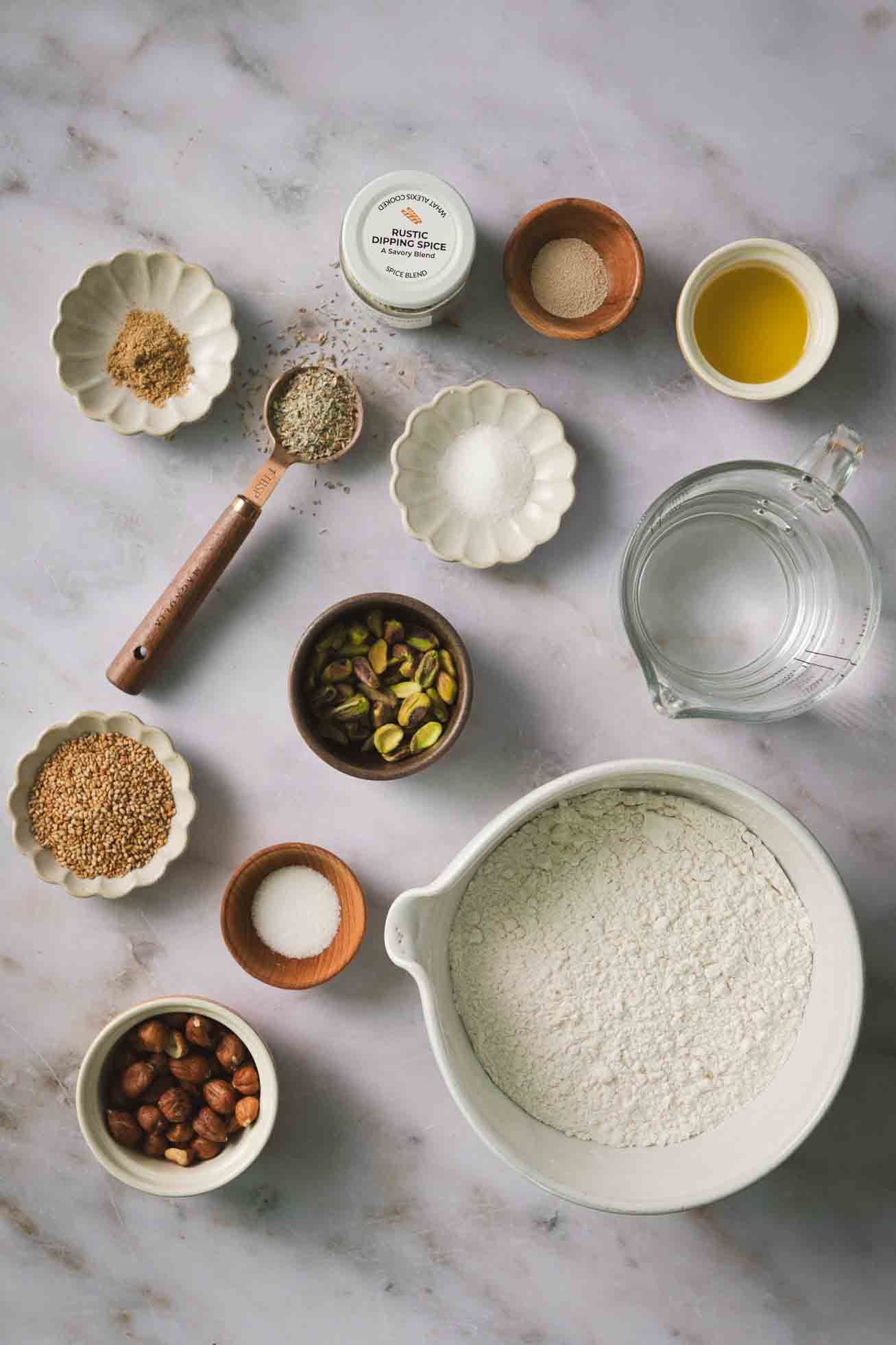 Ingredients for baking laid out on marble countertop including flour, nuts, seeds, and measuring bowls.