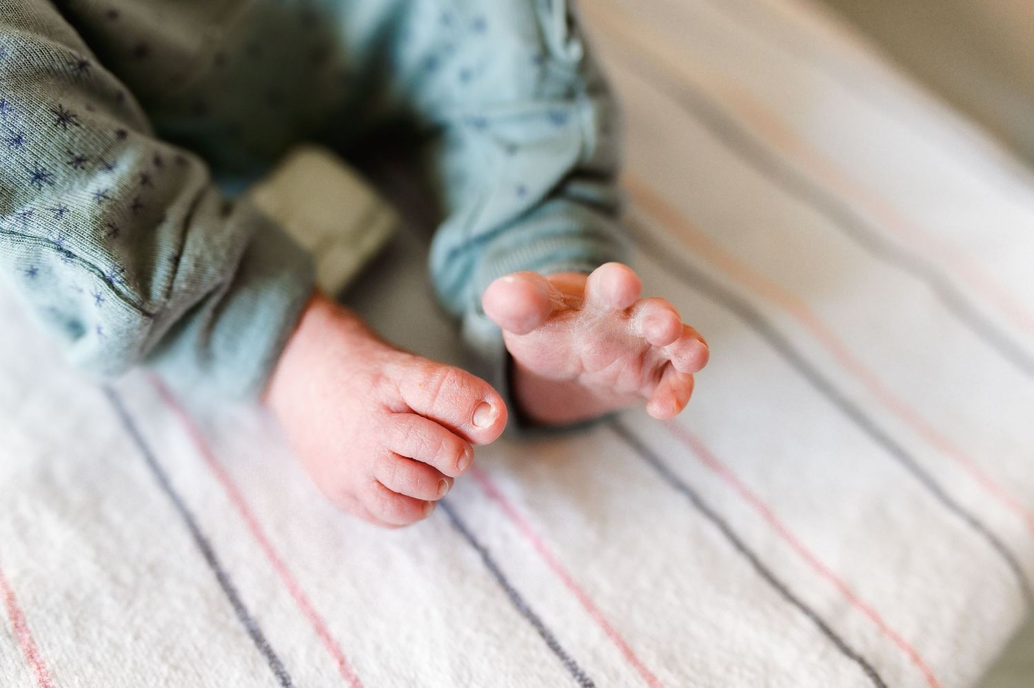 Close-up photo of tiny baby feet resting on striped bedding in soft natural light.