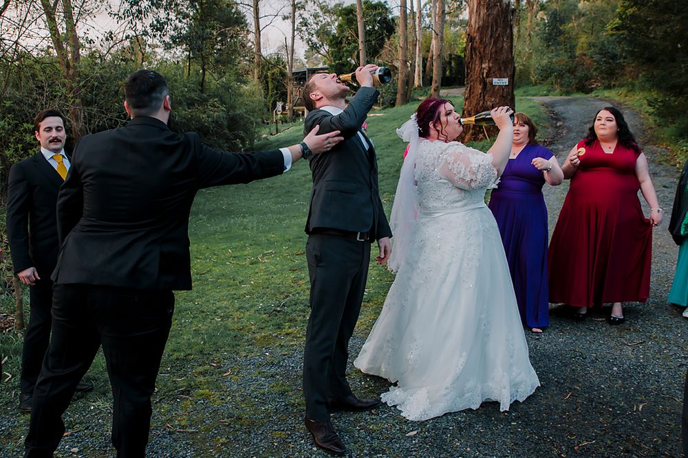Wedding party celebrates together with hugs and embraces on a scenic outdoor path during autumn.