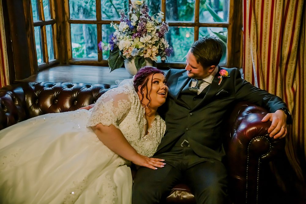 A couple shares an intimate moment while embracing and dancing together with vines and decor visible in the background.