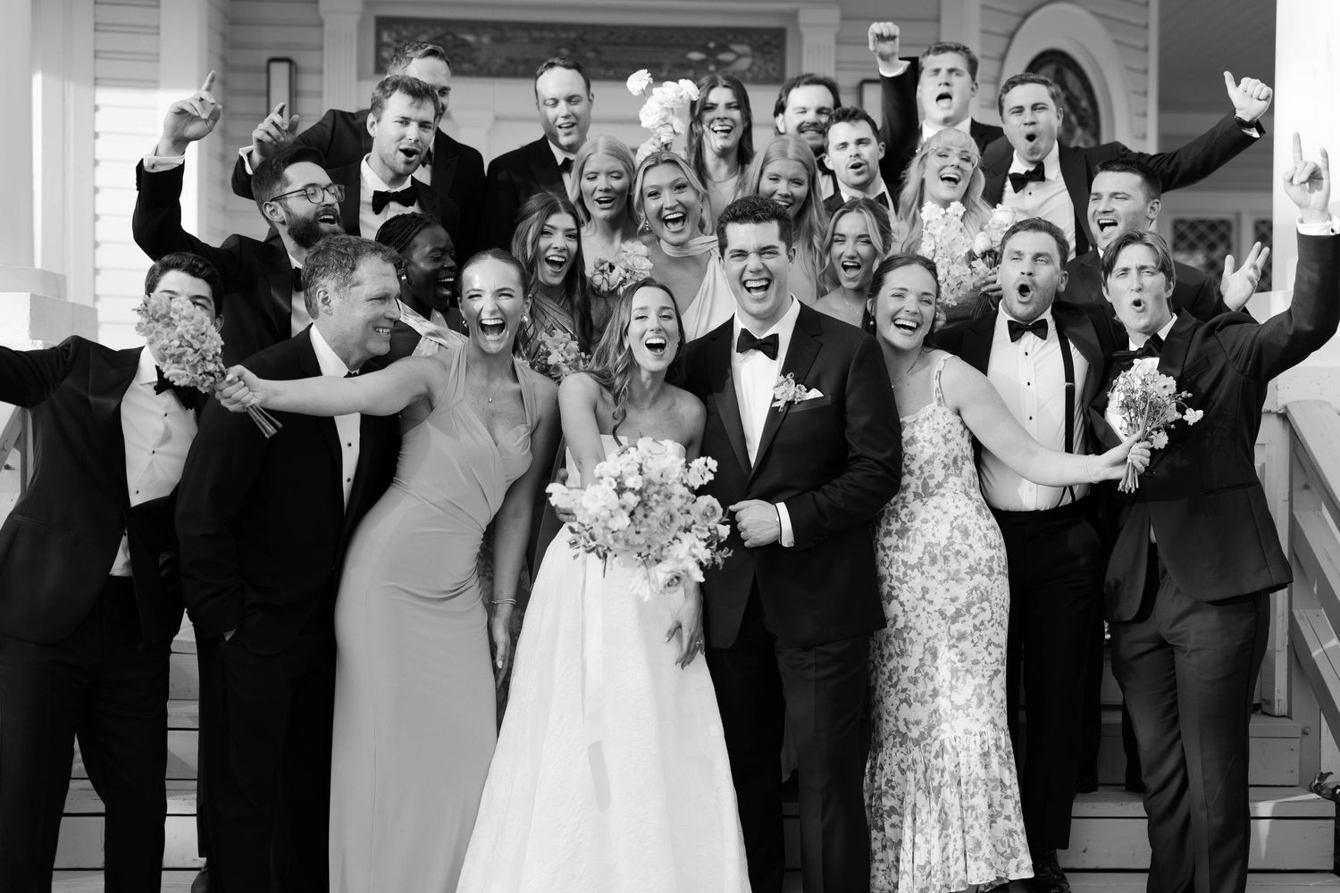 A joyful wedding party poses together in a classic black and white group photograph.