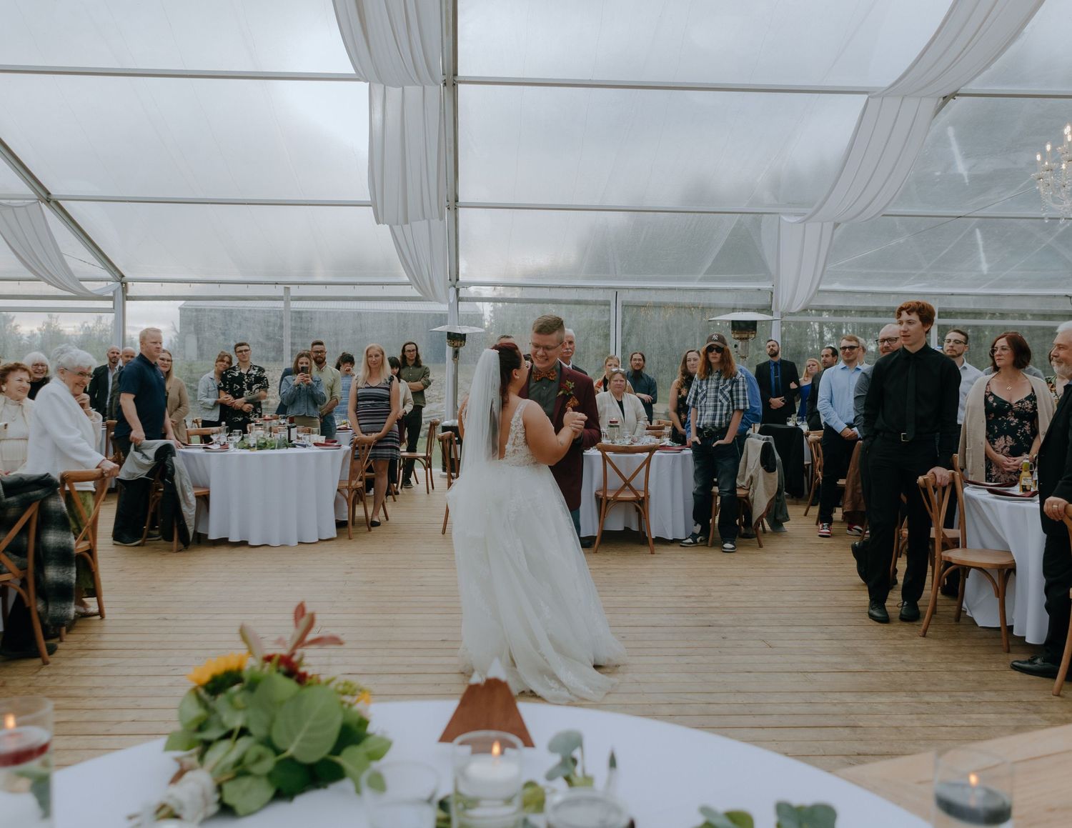 Wedding reception celebration inside a bright white tent with guests seated at round tables.