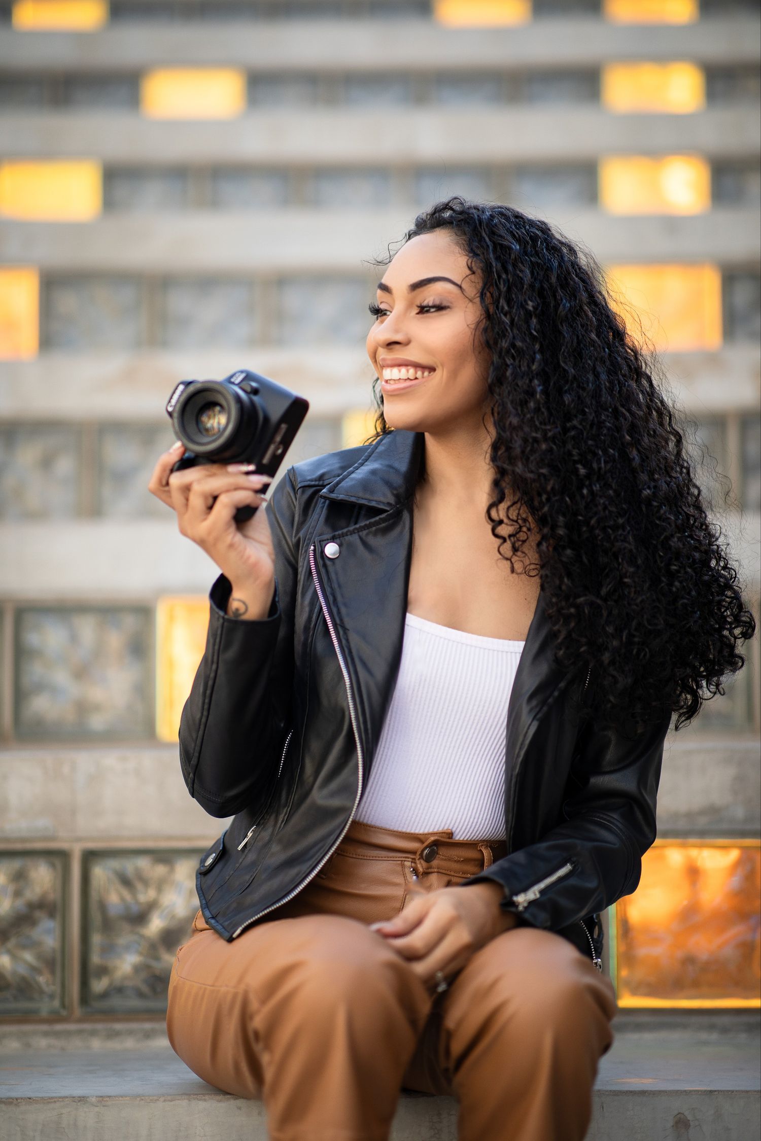 Photographer in leather jacket reviews photos on camera while sitting on outdoor steps.