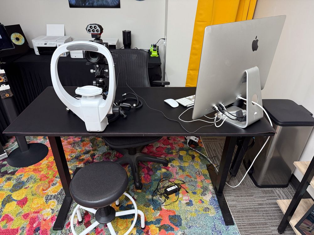 Modern home office setup with iMac computer, gaming headset, and colorful patterned rug on black desk.