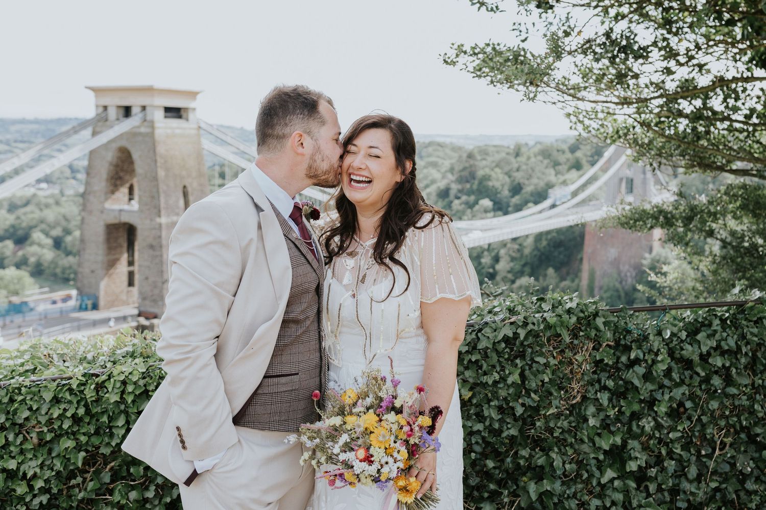 A joyful wedding moment captured at the Clifton Suspension Bridge in Bristol with a colorful bouquet and scenic backdrop.
